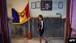 Un copil trece pe lângă un portret al fostului dictator comunist Nicolae Ceaușescu și un steag al României socialiste expuse pentru vizitatori la „Apollo Baths” – un muzeu privat din Baile Herculane.