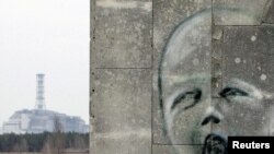 Ýüzün surat çekilen diwaryň arkasynda Çernobyl atom elektrik stansiýasyndaky 4-nji reaktoryň üstüni örtýän sarkofag görünýär, 4-nji aprel.