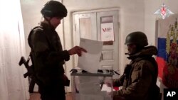 Зображення з відео, яке опублікувала пресслужба Міноборони Росії в середу, 13 березня 2024. Російський військовослужбовець віддає свій бюлетень під час незаконного голосування на виборах президента Росії в окупованій частині Донецької області