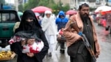 An Afghan woman walks through a market as a Taliban fighter stands guard in Kabul. (file photo)