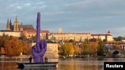 Lucrare de David Černý, despre care artistul spune că e o reacție la actuala situație politică din Cehia și la alegerile din 25-26 octombrie, la fel ca locul unde e amplasată, arătînd spre Castelul din Praga, unde se află reședința prezidențială.