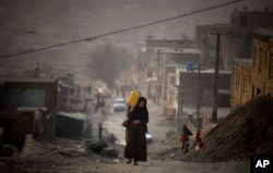 A woman carries water in a plastic container as she ascends a slope on the way toward her home in Kabul. (file photo)