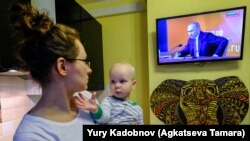 A woman holds her son as she watches a TV broadcast of Russian President Vladimir Putin's annual press conference in Moscow on December 14. 